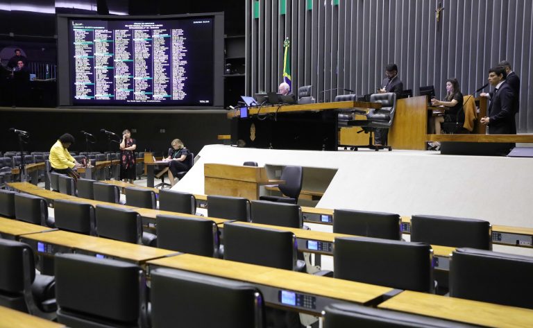 Parlamentares e suas atividades legislativas no Congresso Nacional. Imagem do Plenário da Câmara dos Deputados com o painel de votações ligado. Ambiente meio vazio. Alguns parlamentares na mesa diretora.